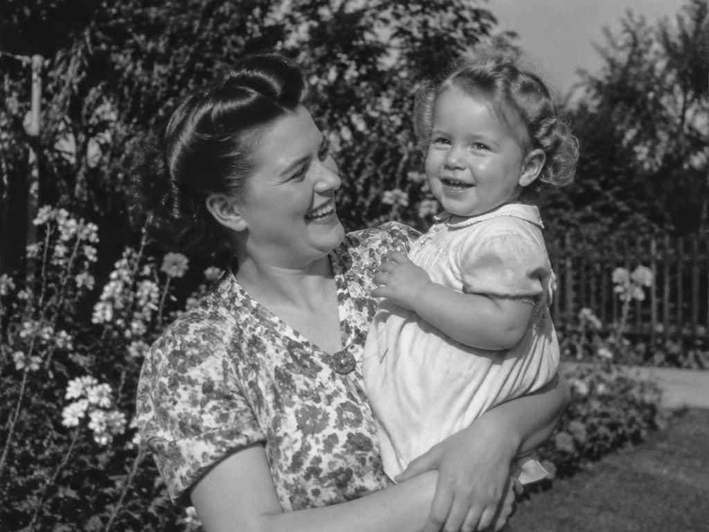 Before: black and white photograph of a smiling mother holding her small child in a flower garden